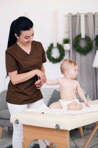 一位职业女性女按摩师对小宝宝进行按摩。在现代舒适的房间里, 孩子们在沙发上按摩