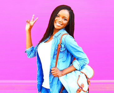 快乐的年轻非洲妇女与背包在粉红色背景