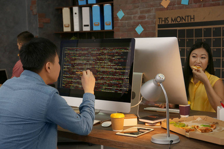 在办公室工作的年轻程序员吃比萨饼照片