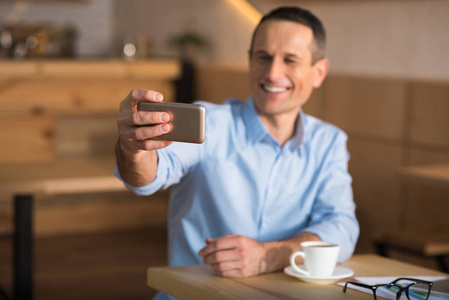 微笑的商人采取自拍与智能手机在咖啡馆