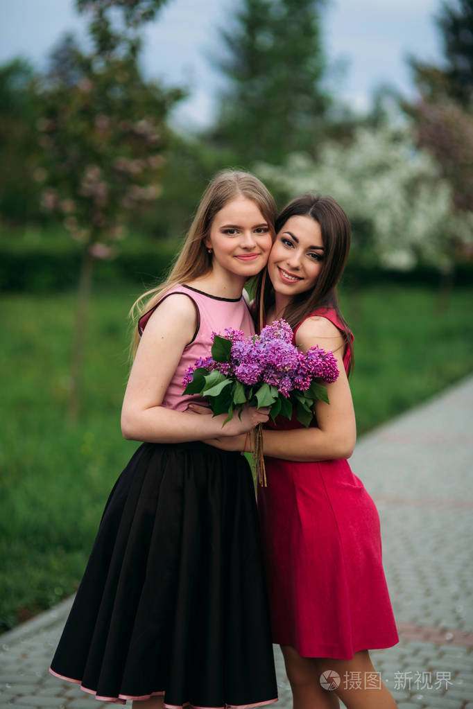 两姐妹为摄影师摆姿势微笑的魅力和漂亮女孩开花的树春天樱花