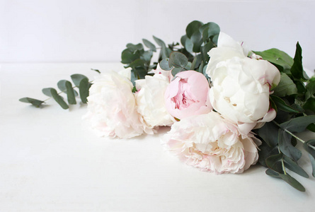 风格的股票照片。装饰静物花的构图。婚礼或生日花束的粉红色和白色牡丹花和桉树枝。白色表背景