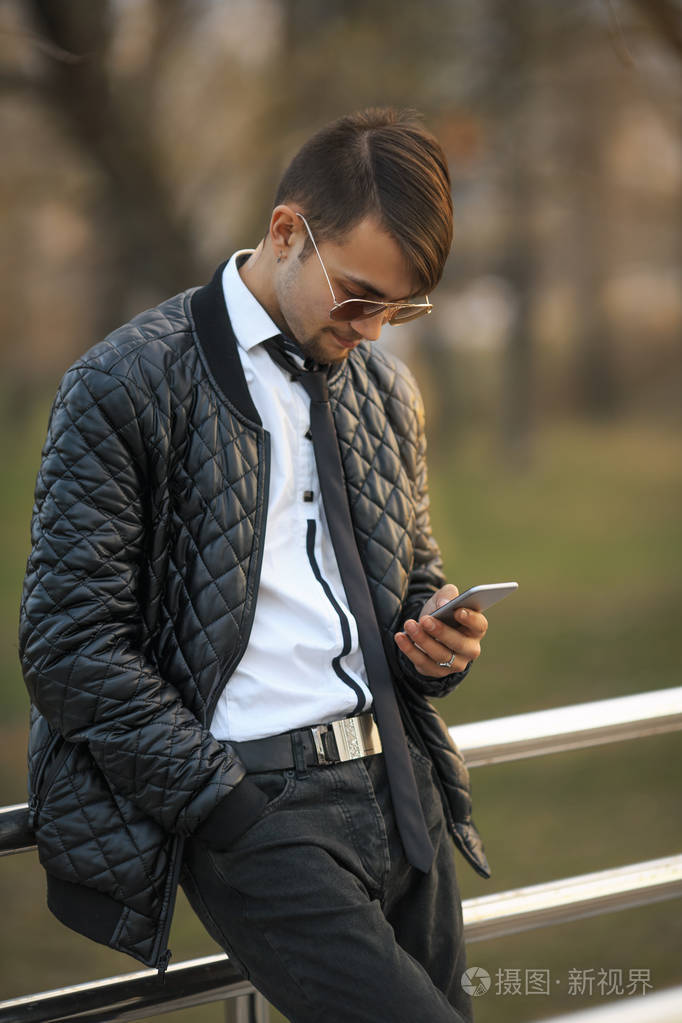 portret 的年轻白人帅哥与现代发型在飞行员太阳镜和智能手机在日落时