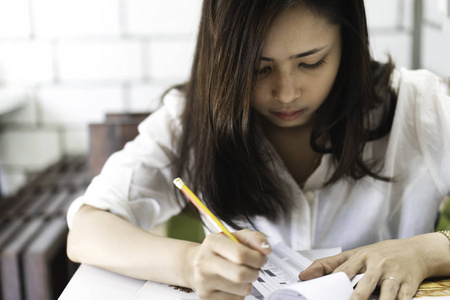 有魅力的亚洲年轻女子用铅笔在咖啡馆里写论文。美丽的女性看着餐厅菜单, 并选择和决定什么订购