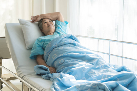 亚洲郁闷的老年妇女病人躺在床上, 望着窗外的医院。老年妇女因患病而高兴康复