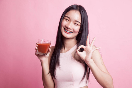 年轻的亚洲妇女显示在粉红色的背景番茄汁确定