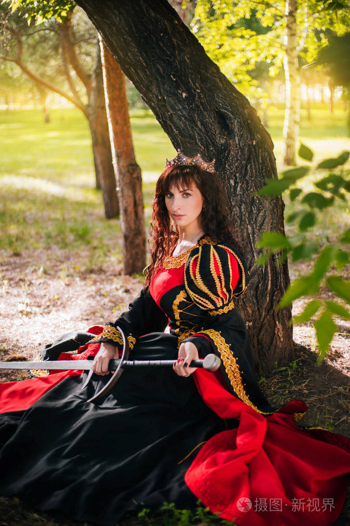 王后手里拿着一把剑在皇冠上的漂亮女孩幻想中世纪黑色和红色礼服与金