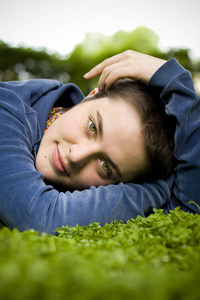 肖像的短头发和绿色眼睛的漂亮女孩躺在草地上，微笑着，看着相机