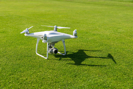 白色专业 quadcopter 无人机摄像机从上面对绿色草在背景