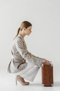 时尚的年轻女性旅行者在亚麻夹克的侧面视图打开老式手提箱在灰色背景下隔离