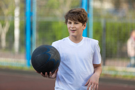 可爱的年轻体育男孩在运动场上打篮球在春天或夏天假日