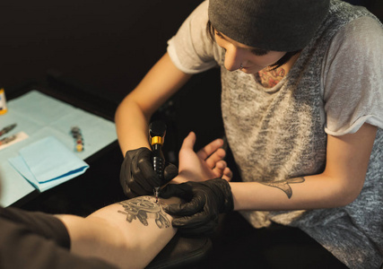 年轻女子 tattooist 在男性手臂上做纹身