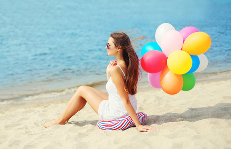 美丽的年轻女子，与五颜六色的气球坐在海滩上