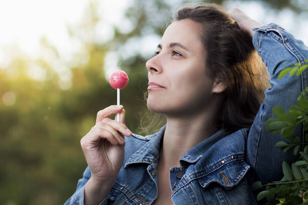 年轻漂亮的女人在公园的棍子上舔一根冰柱上的焦糖糖。一个 Chupa Chups 的女孩在露天