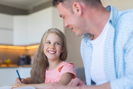 微笑的爸爸与一个小女儿做家庭作业在厨房里