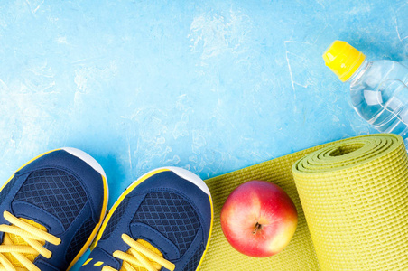 瑜伽垫，运动鞋，苹果，蓝色背景上的瓶水。概念的健康生活方式 健康食品 运动和饮食。运动器材