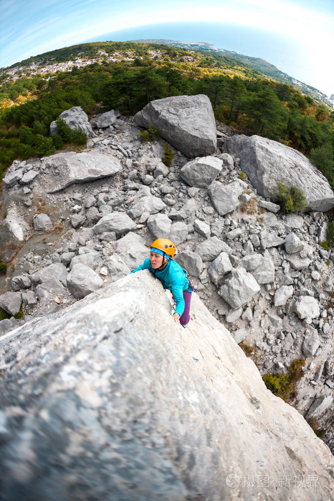 在海上海岸的背景下, 在头盔的登山运动员.一个女人爬上岩石.大自然中