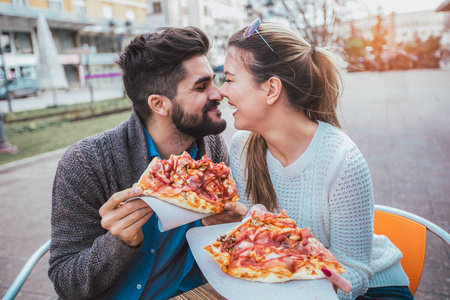 夫妇吃比萨饼在户外和微笑。他们在咖啡馆里分享比萨饼。