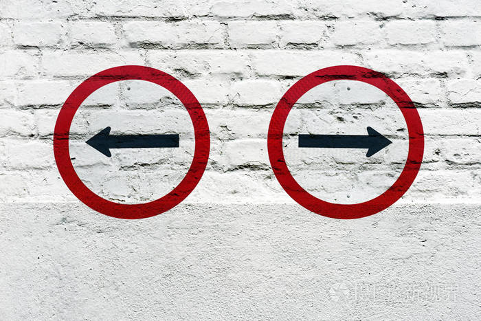 在白色砖墙上加盖的相反位置的定向交通标志