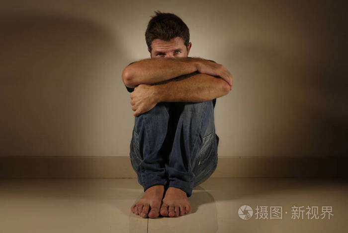 年轻绝望和沮丧的人独自哭泣坐在家里地板上的阴暗和戏剧性的工作室光