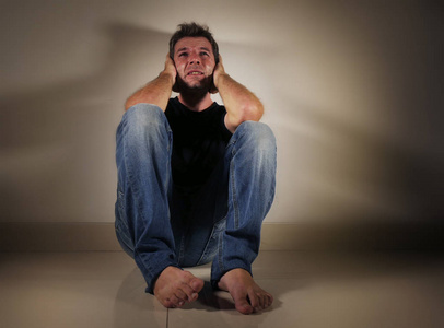 年轻绝望和沮丧的人独自哭泣坐在家里地板上的阴暗和戏剧性的工作室光