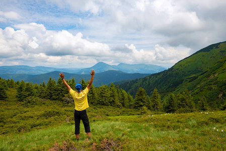 冒险家张开双臂站在绿色的山草甸上, 欣赏着绵延地平线的绿色山林之山的全景。史诗般的旅行在山上。后视图, 广角