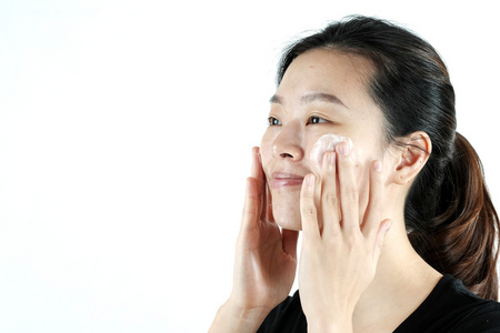 可爱的亚洲女孩在脸上涂抹奶油乳液，与白色隔离