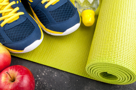 瑜伽垫，运动鞋，苹果，深色背景上的瓶水。概念的健康生活方式 健康饮食 运动和饮食。运动器材