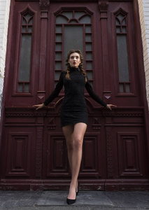 年轻的女孩在黑色礼服附近的老式红门在城市