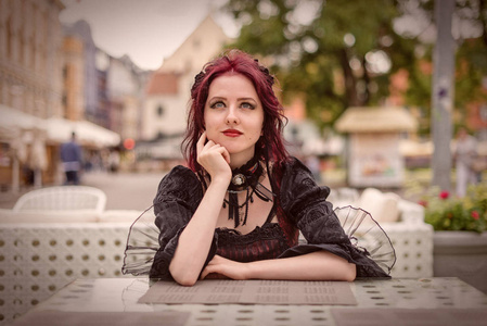 年轻华丽的红头发妇女坐在一个户外咖啡馆穿着复古时尚服装