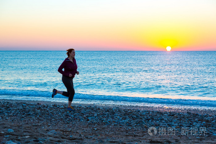 日出时分沿着海冲浪海滩上慢跑的年轻女人