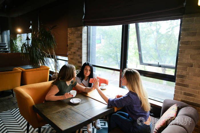 漂亮的女性朋友在咖啡馆里说话使用智能手机喝咖啡