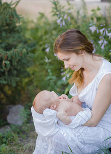 一个美丽的年轻母亲抱着一个婴儿在她的怀里站在花园里