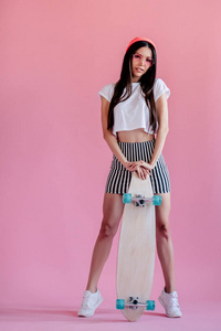 年轻的亚洲少女粉红色背景。有滑板的时尚滑板女孩