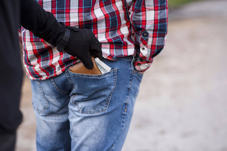 小偷穿着黑色的衣服和手套从口袋里偷钱的钱包.白天在街上扒窃照片