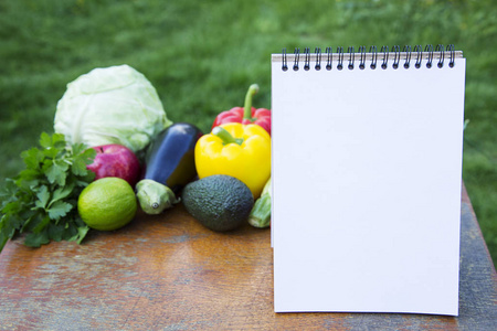 健康食品概念。笔记本和收集不同的水果和蔬菜在木制的餐桌上。侧面视图