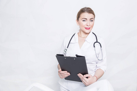 一个女性医生的肖像在白色的医疗睡衣与听诊器持有一个黑色文件夹与病人的音符在光背景下