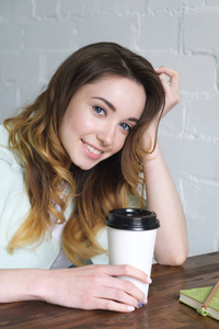 漂亮的小女孩坐在桌边喝咖啡, 头歪着, 微笑着看着镜头。垂直照片