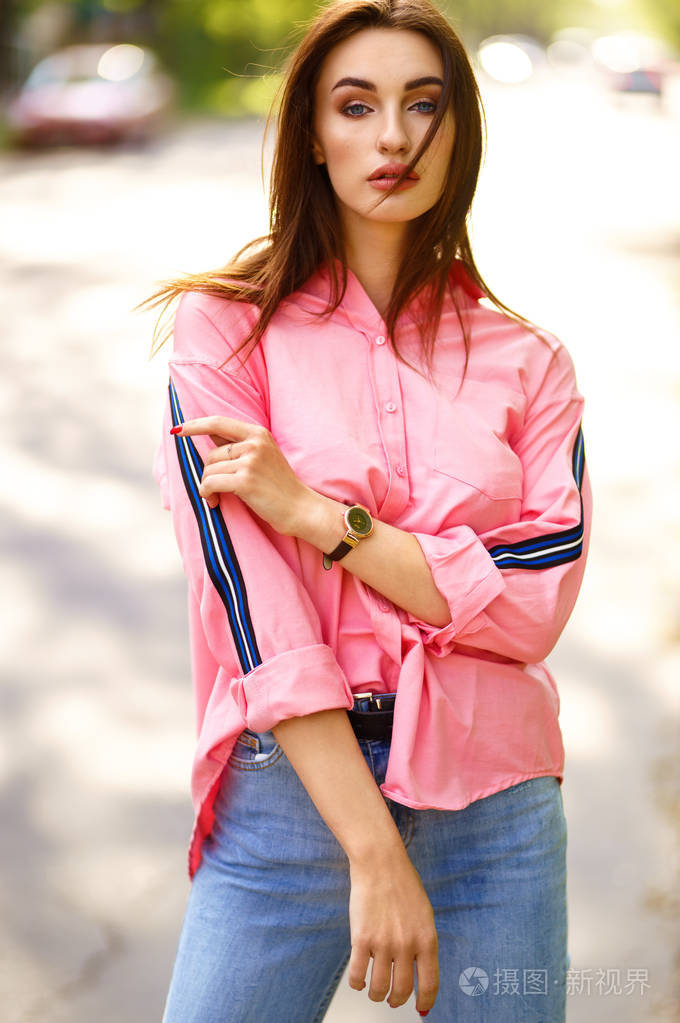 在街上穿着便装的年轻漂亮女人的肖像.穿着粉红色衬衫和牛仔裤.
