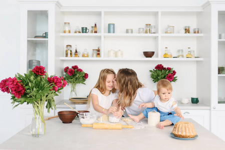 一个年轻的母亲与她的两个孩子正在准备美味和健康的食物在一个大而明亮的厨房。女人教孩子如何做面团