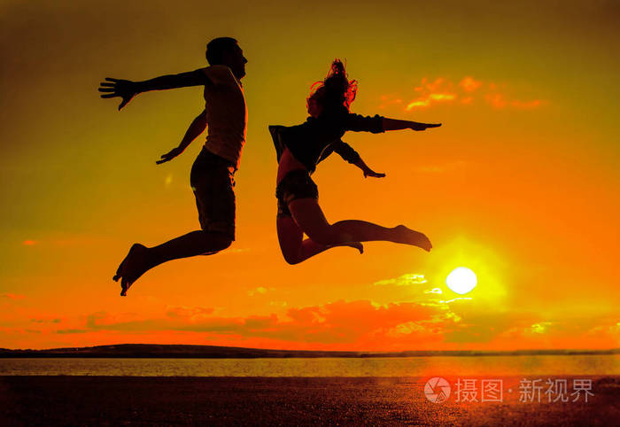 家庭在海滩上.在日落背景下在海滩上跳跃的一对男女的剪影