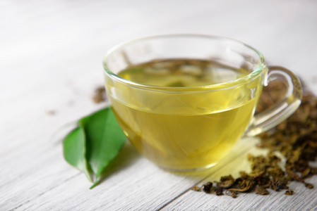 玻璃杯茶绿色的叶子和散的茶周围上木制的灰色背景,关闭照片