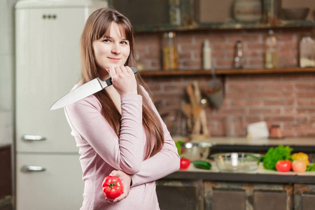 在厨房的桌子旁边一个女人拥有一个西红柿和一把刀，躺下在桌子上新鲜的蔬菜