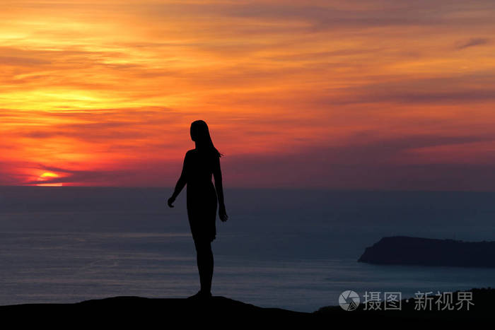 一个女孩站在山上的剪影直接看着美丽的日落和大海的背景