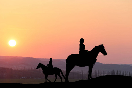 剪影两个女孩骑在一个美丽的日落背景马