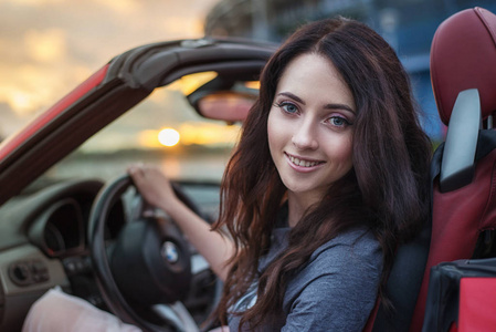 年轻漂亮的黑发女人，在夕阳的余晖驾驶豪华红色敞篷跑车车