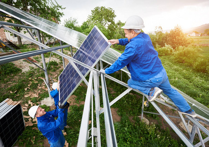安装独立太阳能光电面板系统。三名技术人员组成的团队在绿色夏日景观平台上安装太阳能电池模块。替代能源概念
