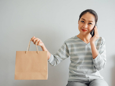 亚洲妇女炫耀她在网上购买的产品的空纸袋。网上购物的概念