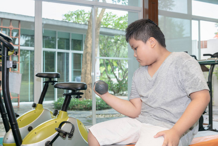 举哑铃男孩肥胖男孩在健身室举哑铃, 锻炼减肥概念照片