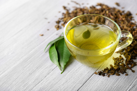 关闭周围玻璃杯茶绿色的叶子和散的茶周围上木制的灰色背景,关闭照片